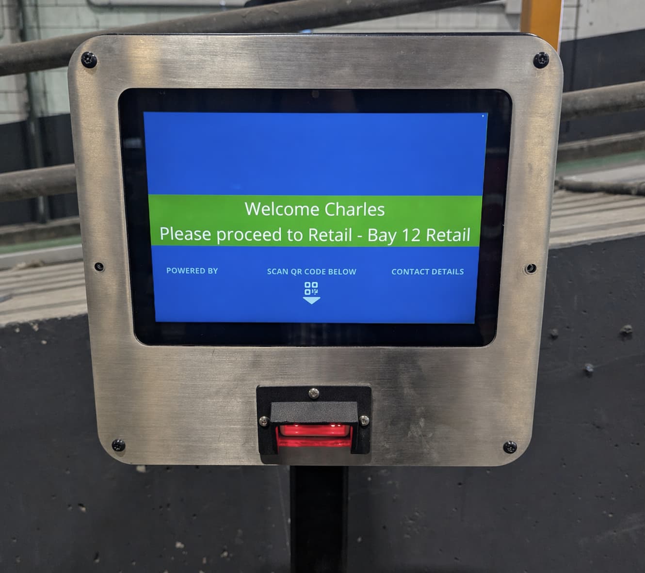 DockSense gate kiosk showing a welcome screen with the driver's name and bay assignment — ‘Welcome Charles, please proceed to Retail – Bay 12’ — above a QR scanner for booking check-in